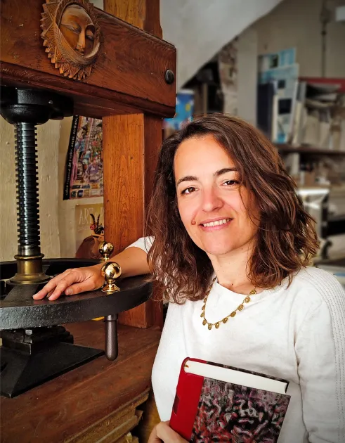 Portrait d’Émilie Gamba dans son atelier, aux côtés d’une presse ancienne et de ses créations.
